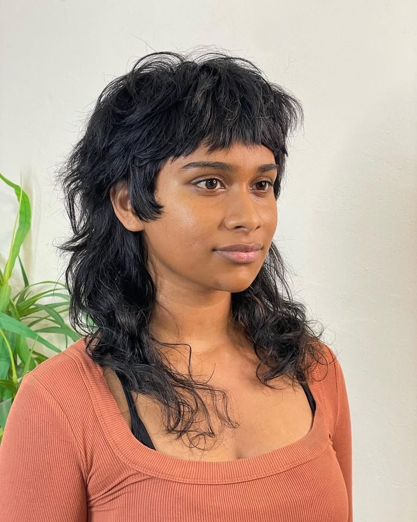 woman with a textured black shag haircut featuring short bangs and layered curls