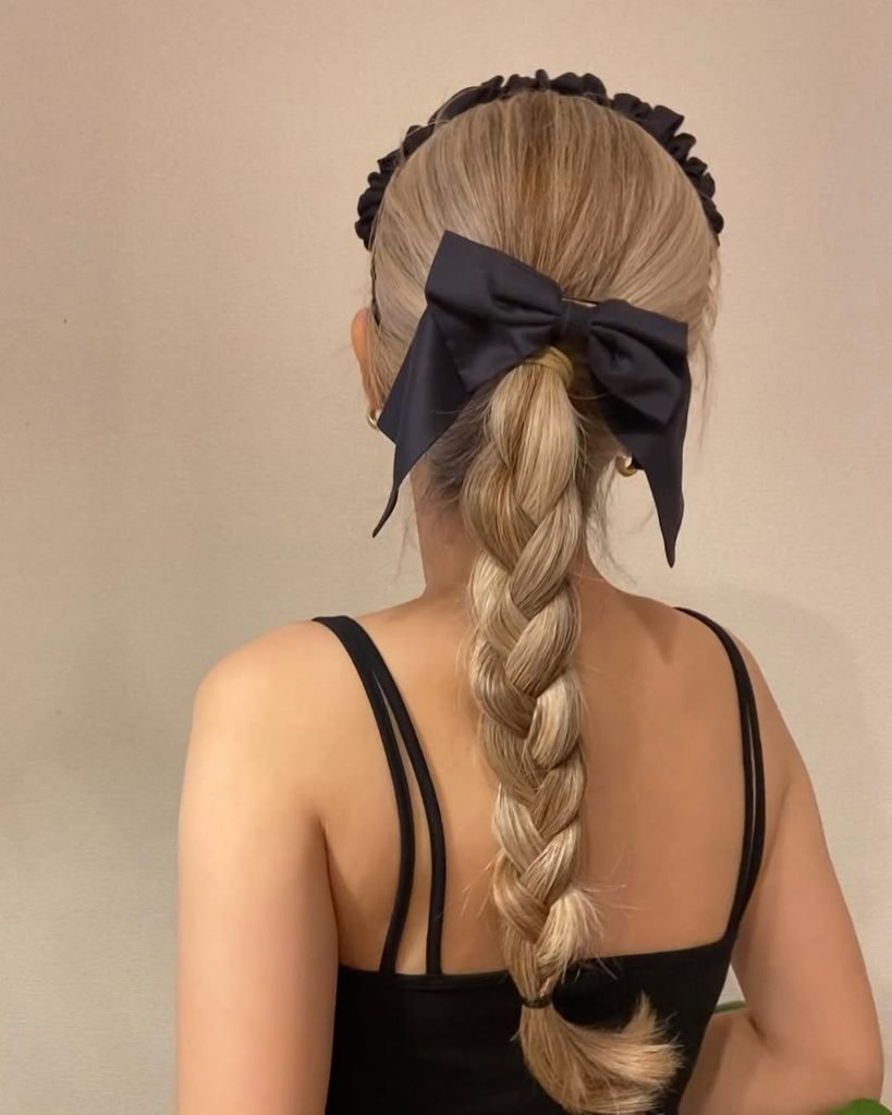 back view of blonde braided ponytail hairstyle accessorized with a large black bow