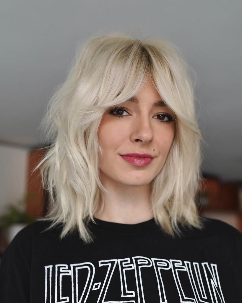 woman with a textured platinum blonde wolf cut hairstyle and middle-parted bangs