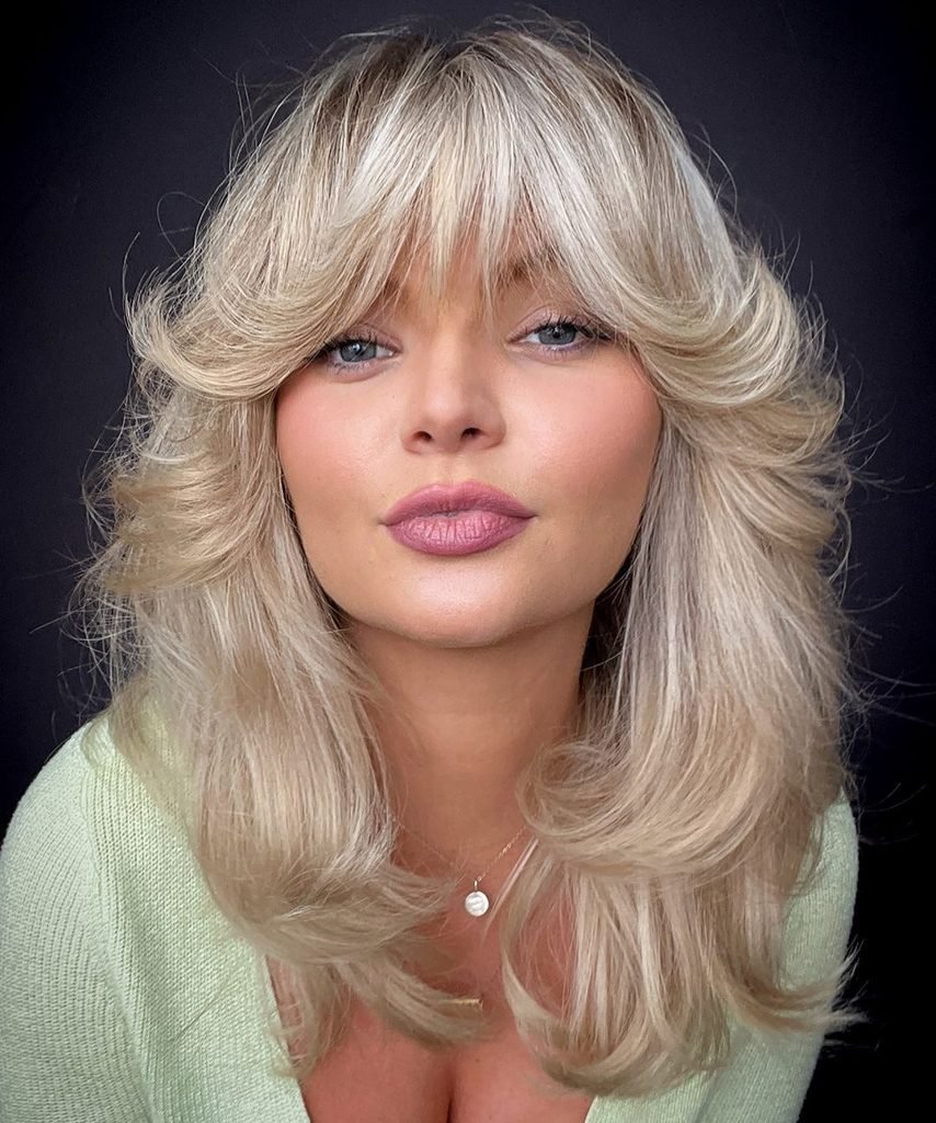 woman with voluminous layered blonde hair and feathered face-framing curtain bangs