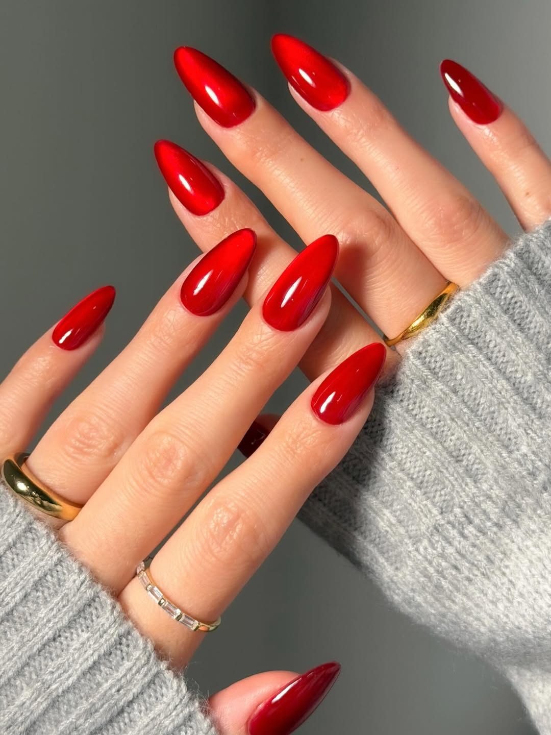 vibrant glossy red almond shaped manicured nails on a person wearing a sweater