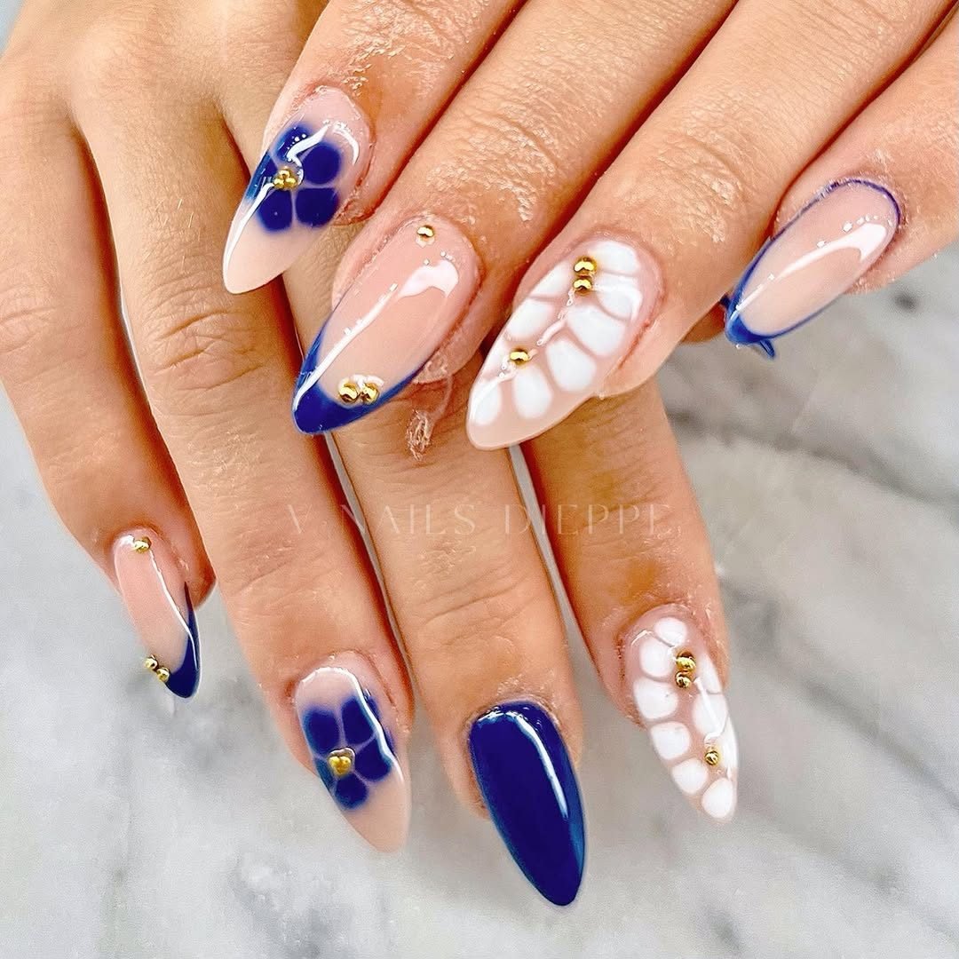 almond shaped manicured nails featuring blue and white floral art accented with small gold beads