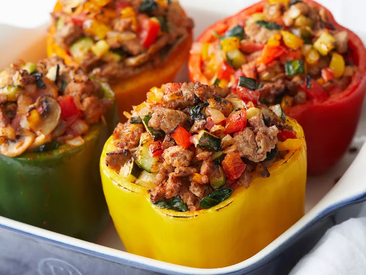 four baked stuffed peppers filled with ground turkey and diced vegetables in a baking dish