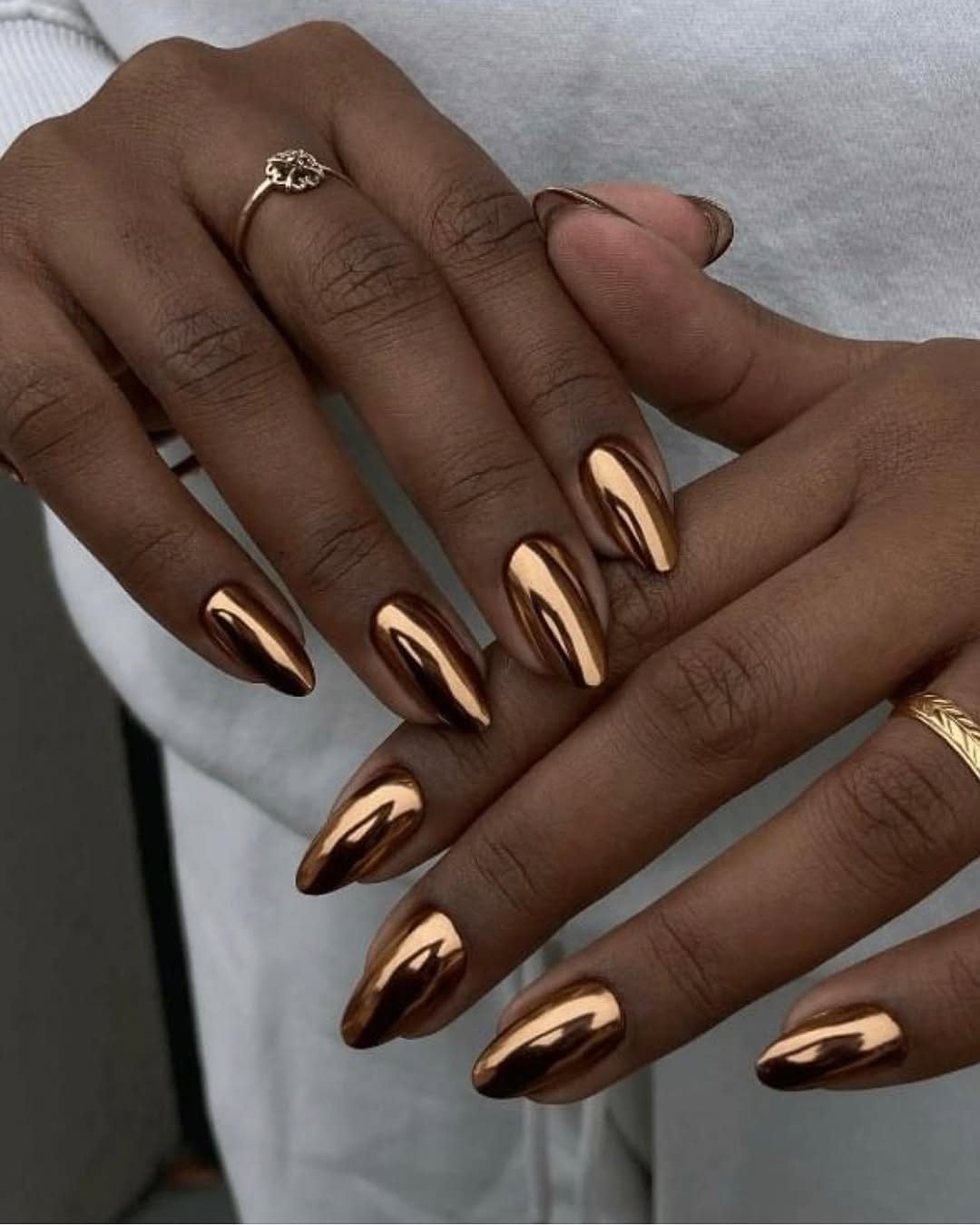 metallic bronze chrome manicure on long almond shaped nails with minimalist gold rings