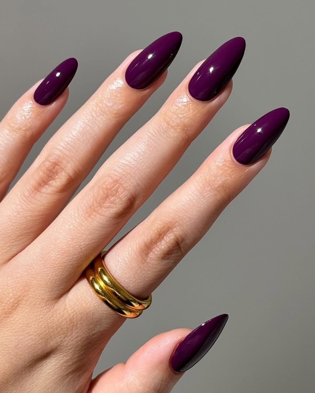 deep plum purple almond shaped manicure on a hand wearing stacked gold rings