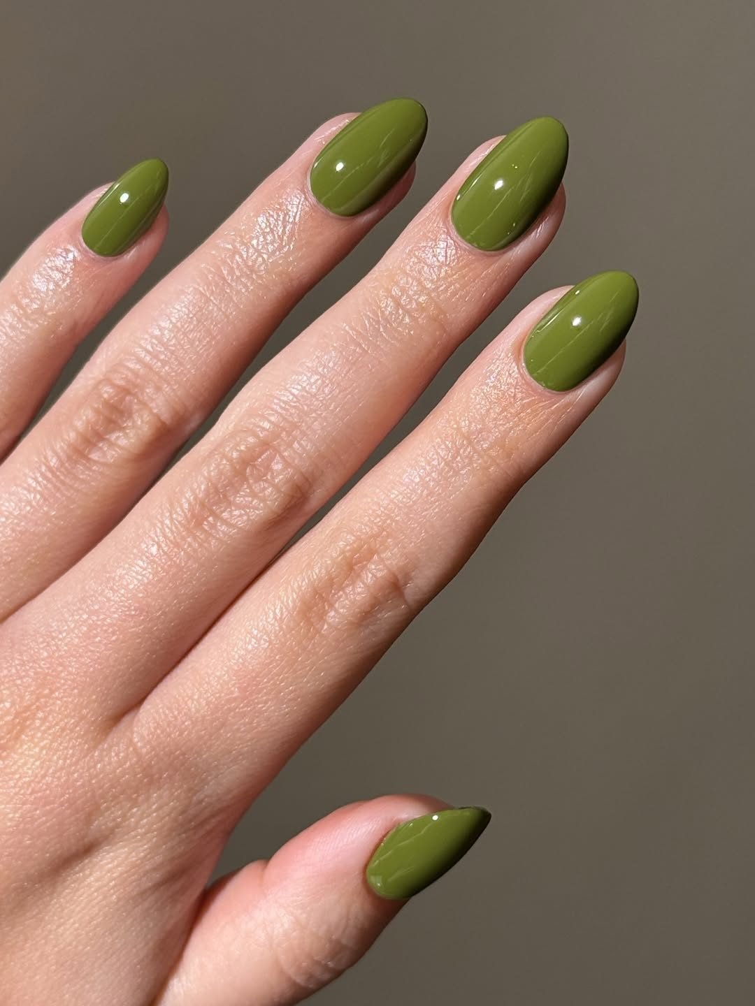 glossy olive green almond shaped manicure on a hand with a neutral background