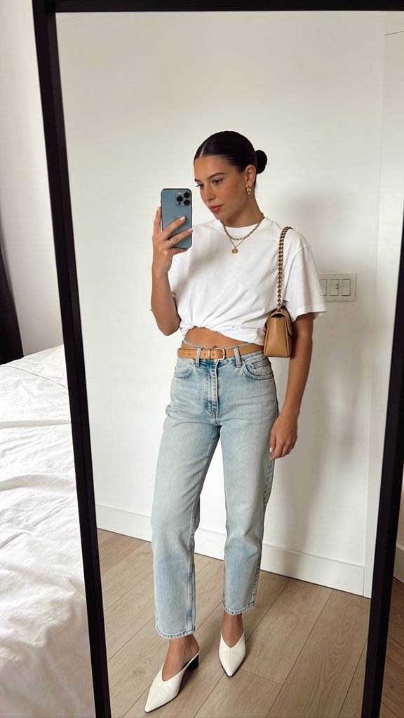 woman in knotted white t-shirt and light blue barrel jeans taking mirror selfie