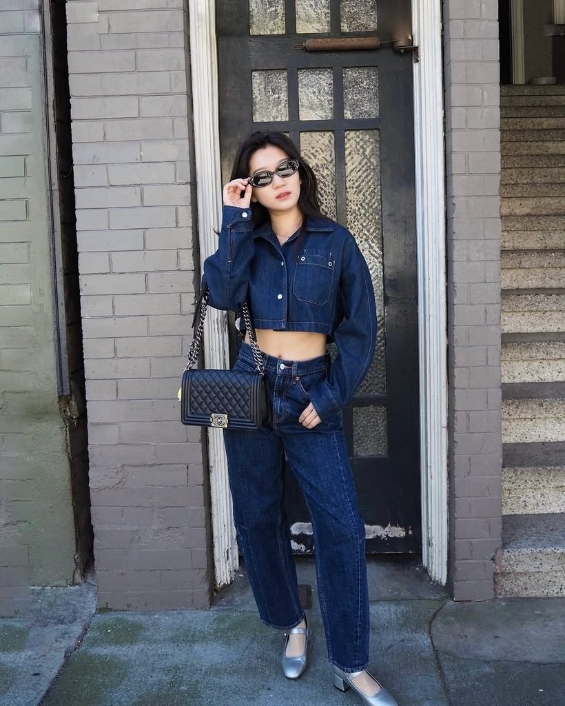 woman in cropped denim jacket and matching blue jeans standing by brick wall