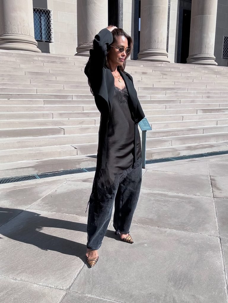 woman wearing black blazer, lace slip dress, and dark barrel jeans on steps