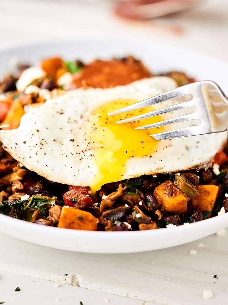 fried egg with a runny yolk over a black bean and sweet potato burrito bowl