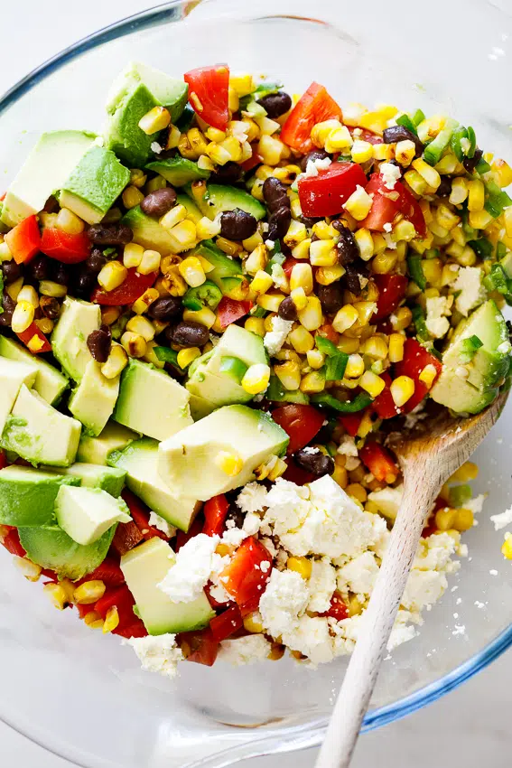 a glass bowl filled with black bean, corn, diced avocado, and feta salad
