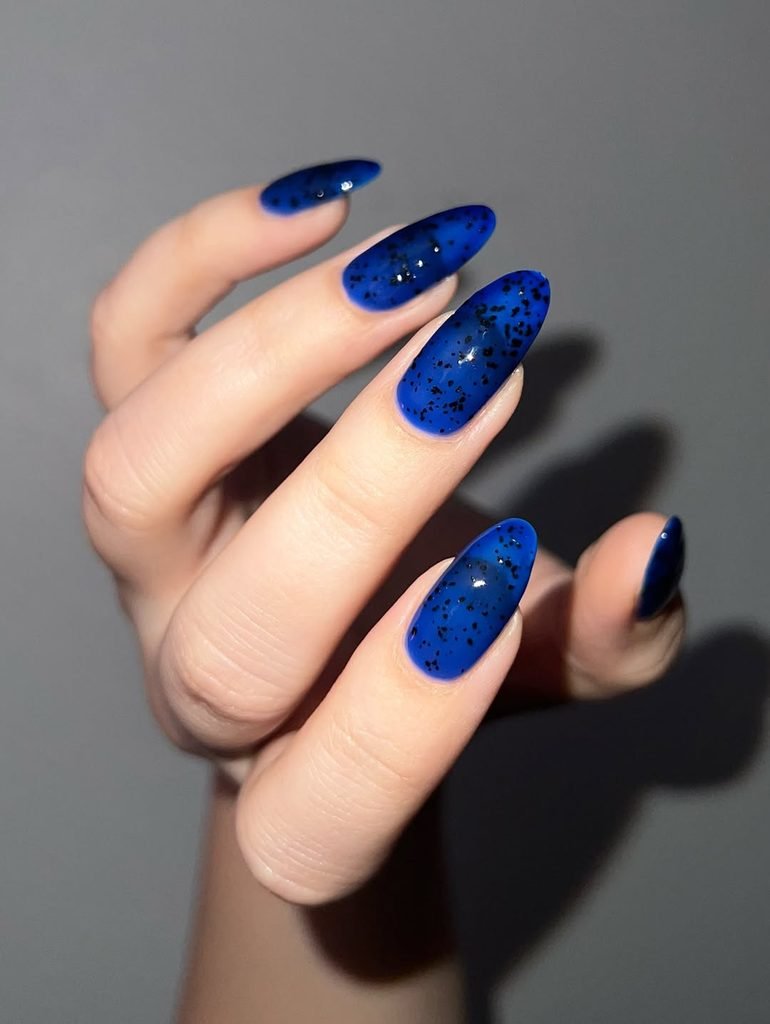 long almond shaped translucent blue nails featuring black speckled glitter accents