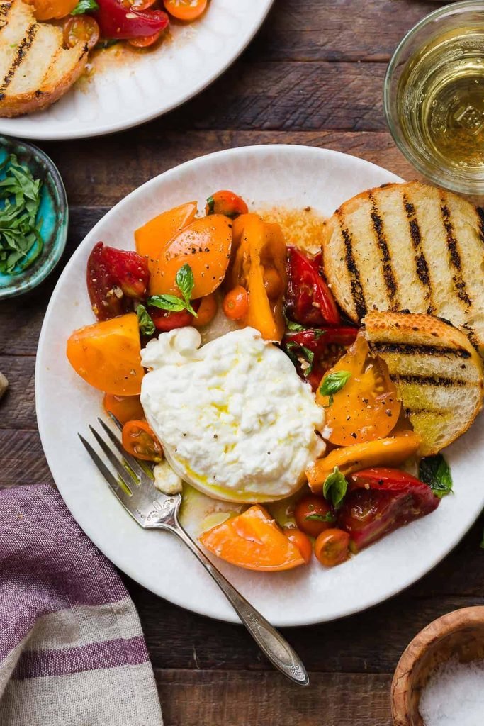 fresh burrata cheese with heirloom tomatoes, basil, and grilled bread on a plate