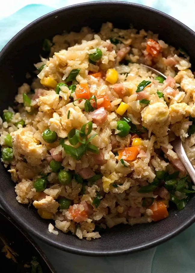 cauliflower fried rice with peas, carrots, corn, and ham in a black bowl