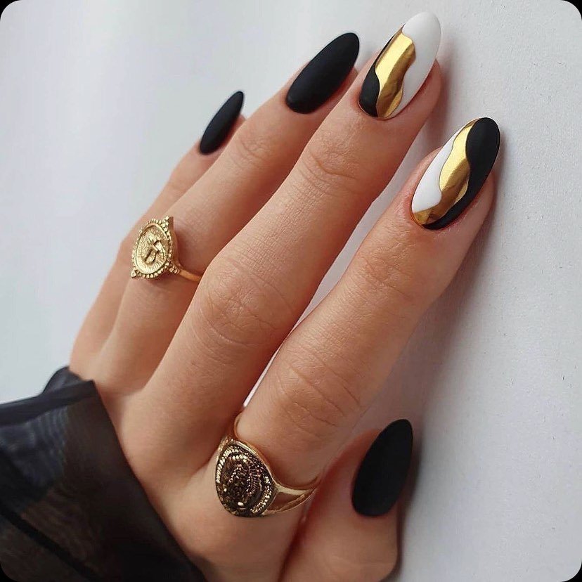 matte black almond nails featuring abstract white and metallic gold swirl accents