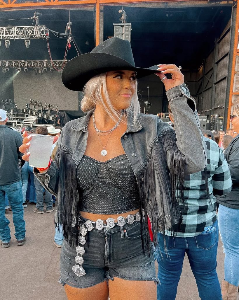 woman in black cowboy hat, fringe denim jacket, and black rhinestone top
