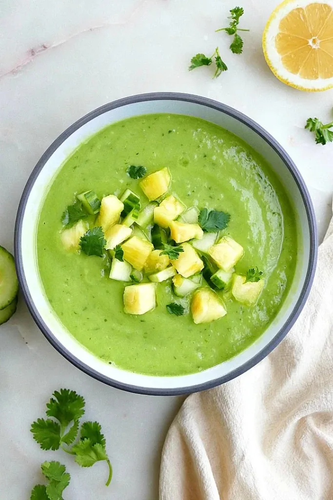 chilled green cucumber avocado soup in a bowl topped with diced pineapple and fresh cilantro