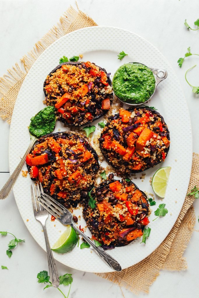 four portobello mushrooms stuffed with vegetable quinoa salad served on a platter with green sauce