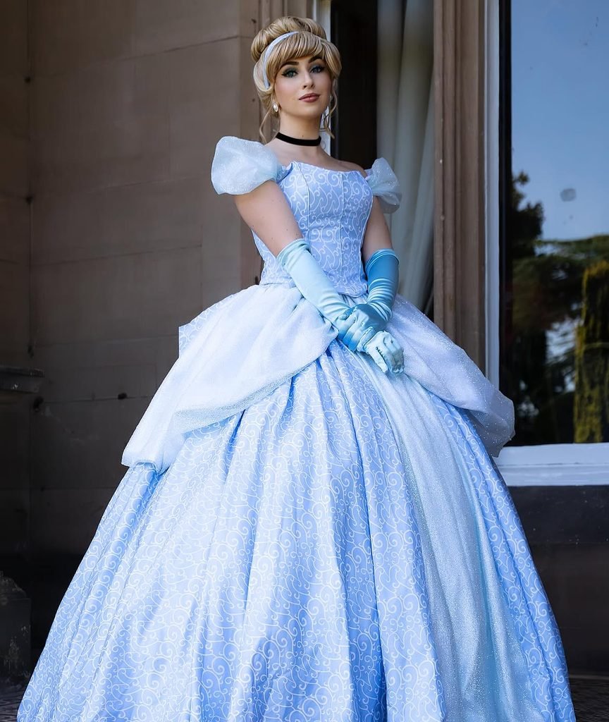 woman in an elaborate blue cinderella ballgown posing by a stone building