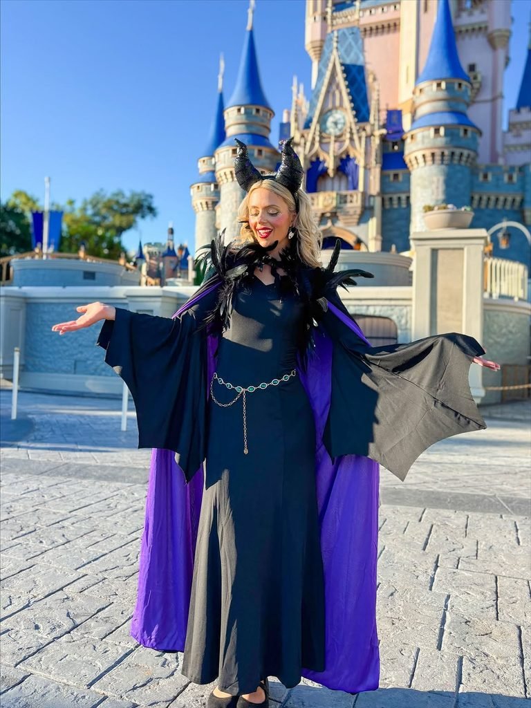 woman in a black and purple gown wearing horns in front of a castle