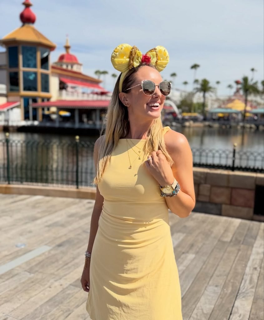 smiling woman wearing a yellow dress and sunglasses on a sunny boardwalk