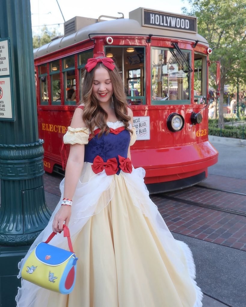 woman wearing a snow white inspired gown smiling next to a red trolley