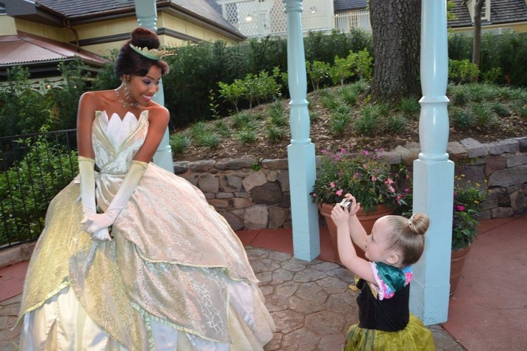 young girl taking a photo of a woman dressed as princess tiana