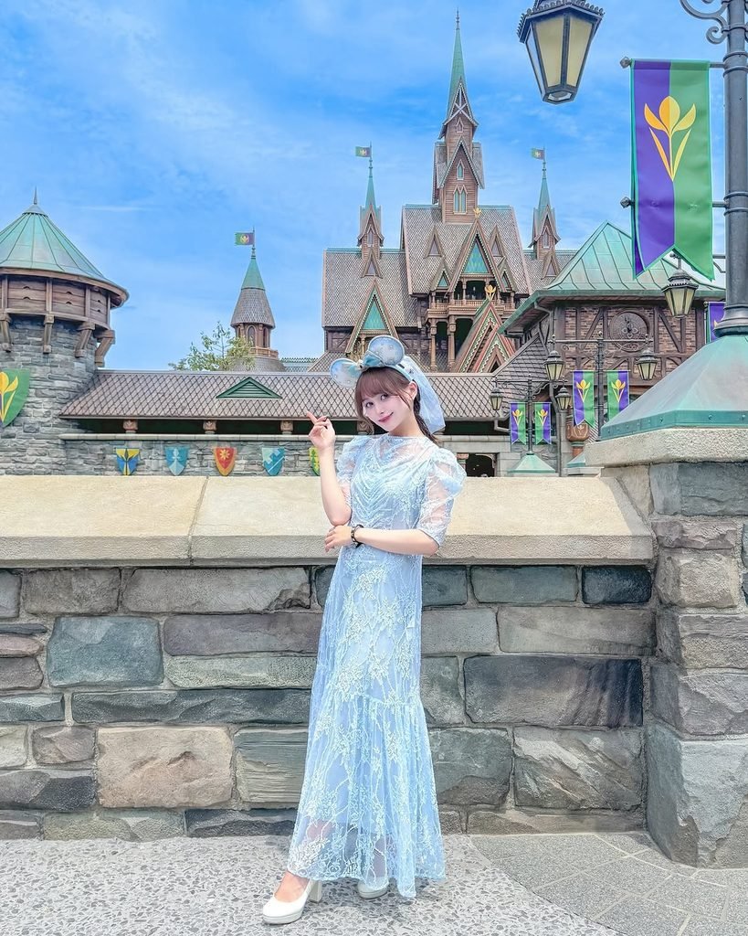 woman in a light blue lace dress posing in front of a large castle