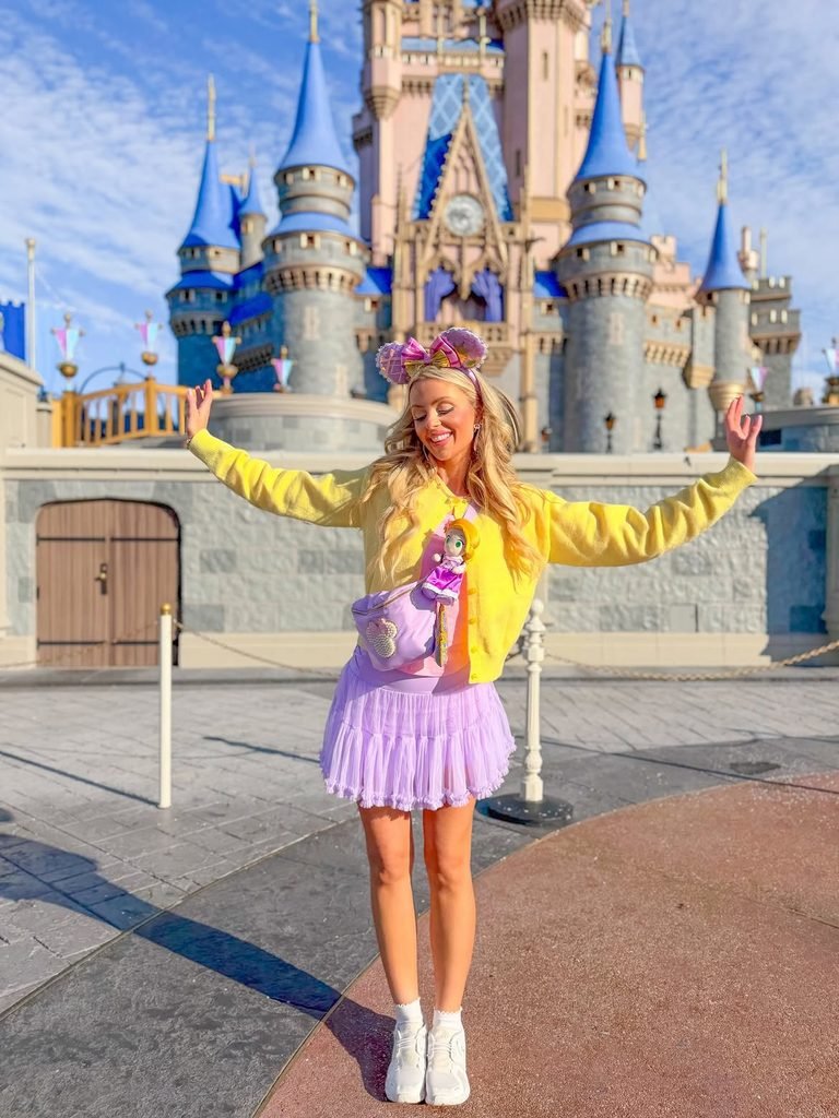 smiling woman in a yellow cardigan and purple skirt before a large castle