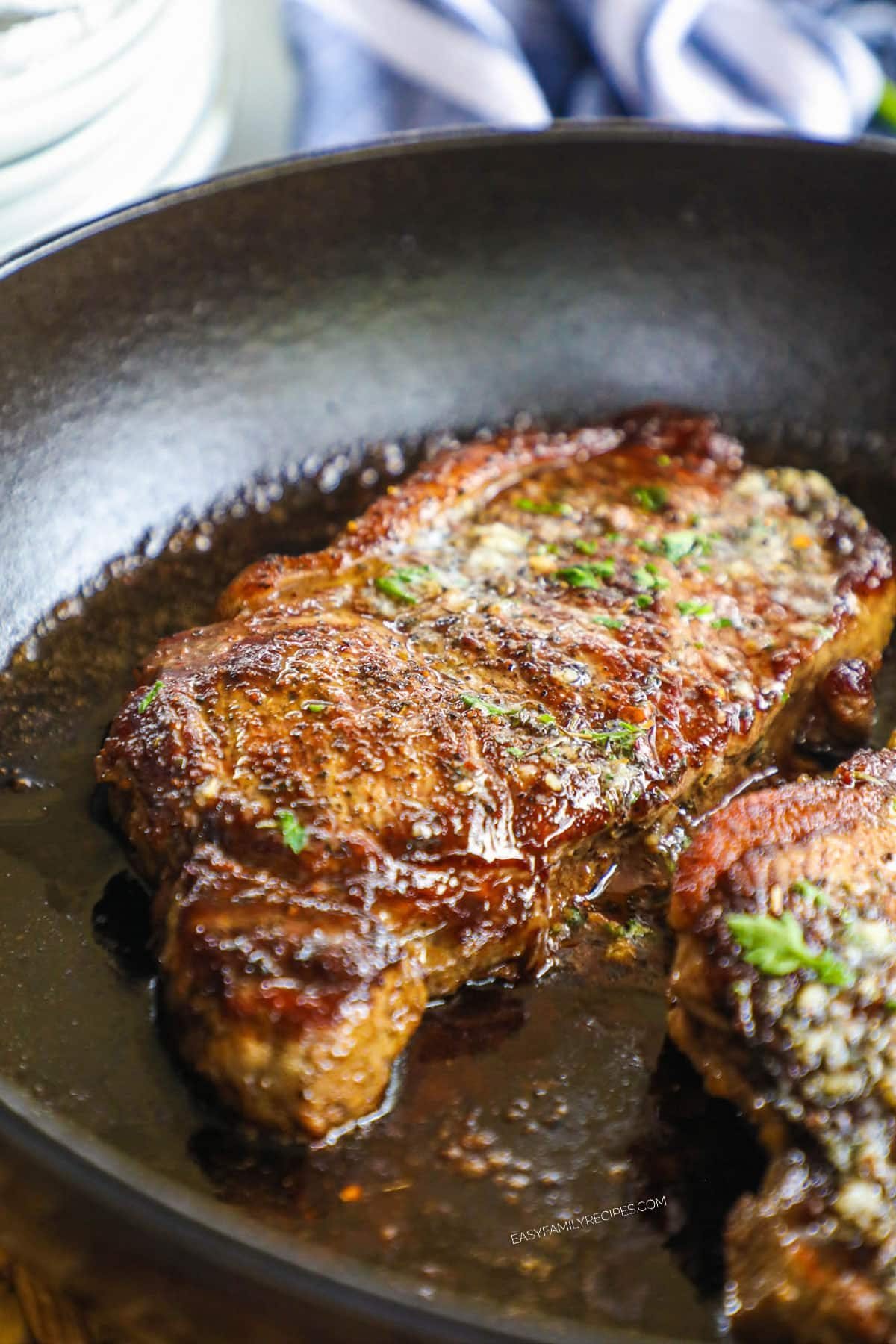 seared cast iron skillet steak topped with melting garlic herb butter and fresh herbs