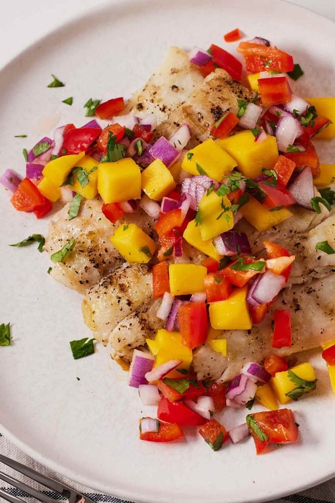 grilled halibut fillet served on a white plate topped with a colorful mango salsa