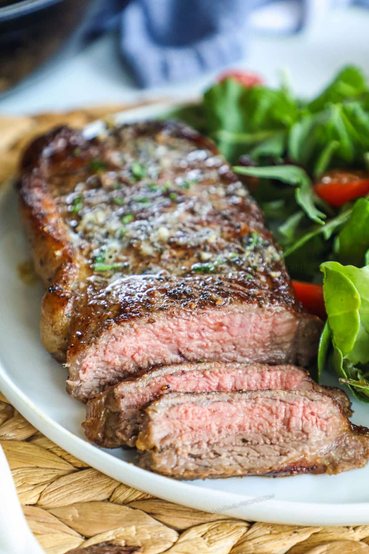sliced medium rare garlic herb butter steak on a plate with fresh green salad
