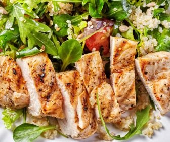 sliced grilled chicken breast served over a fresh green salad with quinoa