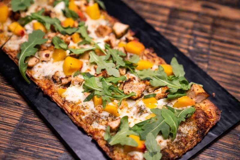 grilled chicken and peach flatbread topped with fresh arugula on a black platter