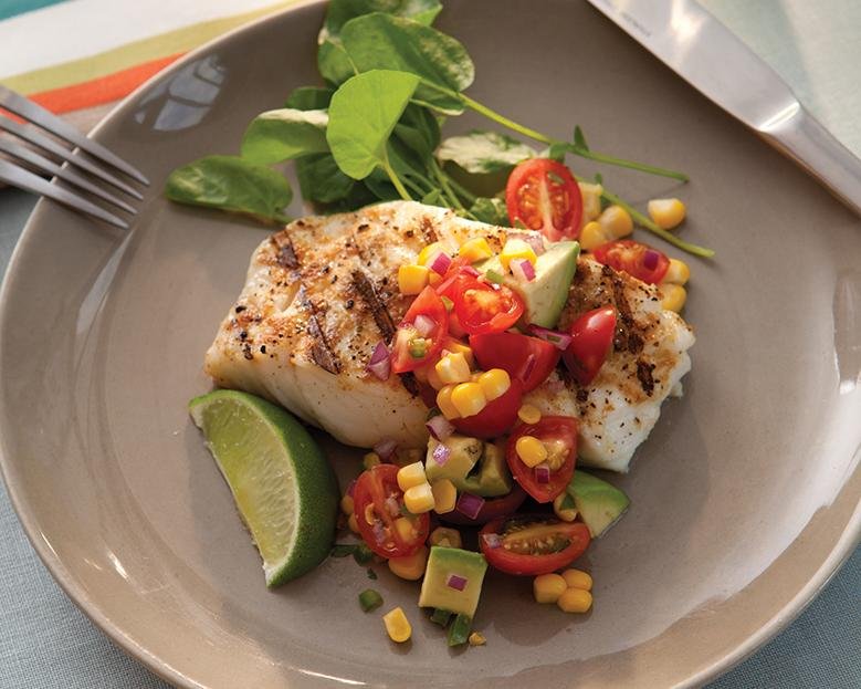 grilled cod fillet topped with a charred corn, tomato, and avocado salad on a grey plate