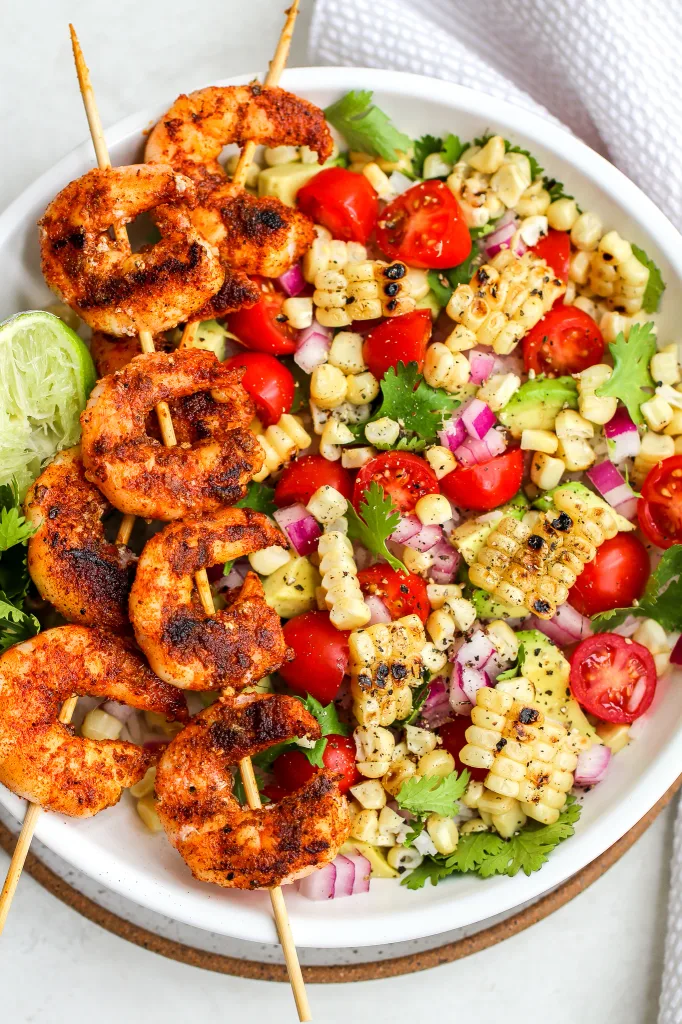 grilled shrimp skewers served over a fresh corn, tomato, and avocado salad