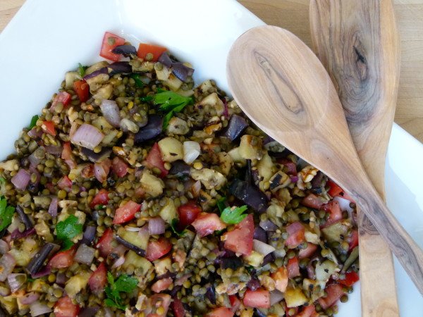 lentil salad with chopped eggplant, tomatoes, onions, and fresh herbs next to wooden spoons