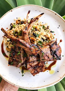 grilled lamb chops served over a bed of couscous salad on a white plate