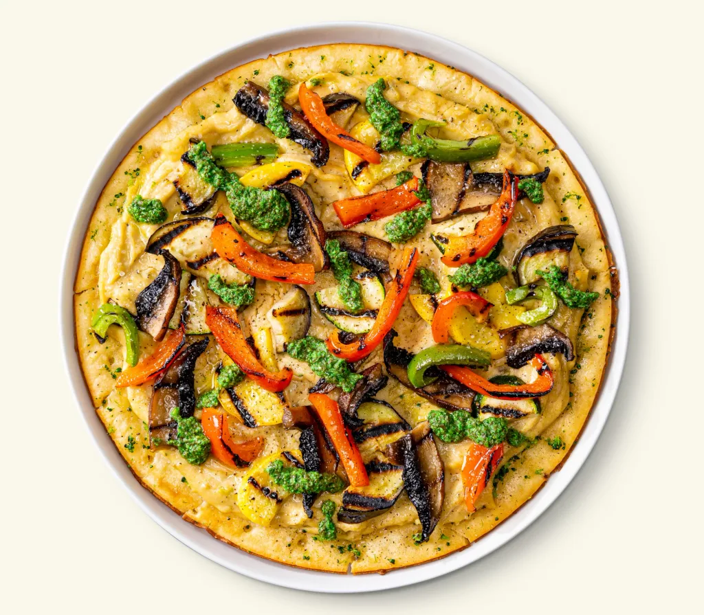 round flatbread pizza topped with grilled peppers, mushrooms, zucchini, and green pesto drops
