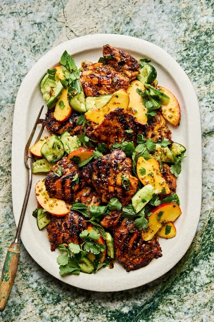 grilled honey mustard chicken served on a platter with sliced peaches, cucumbers, and cilantro