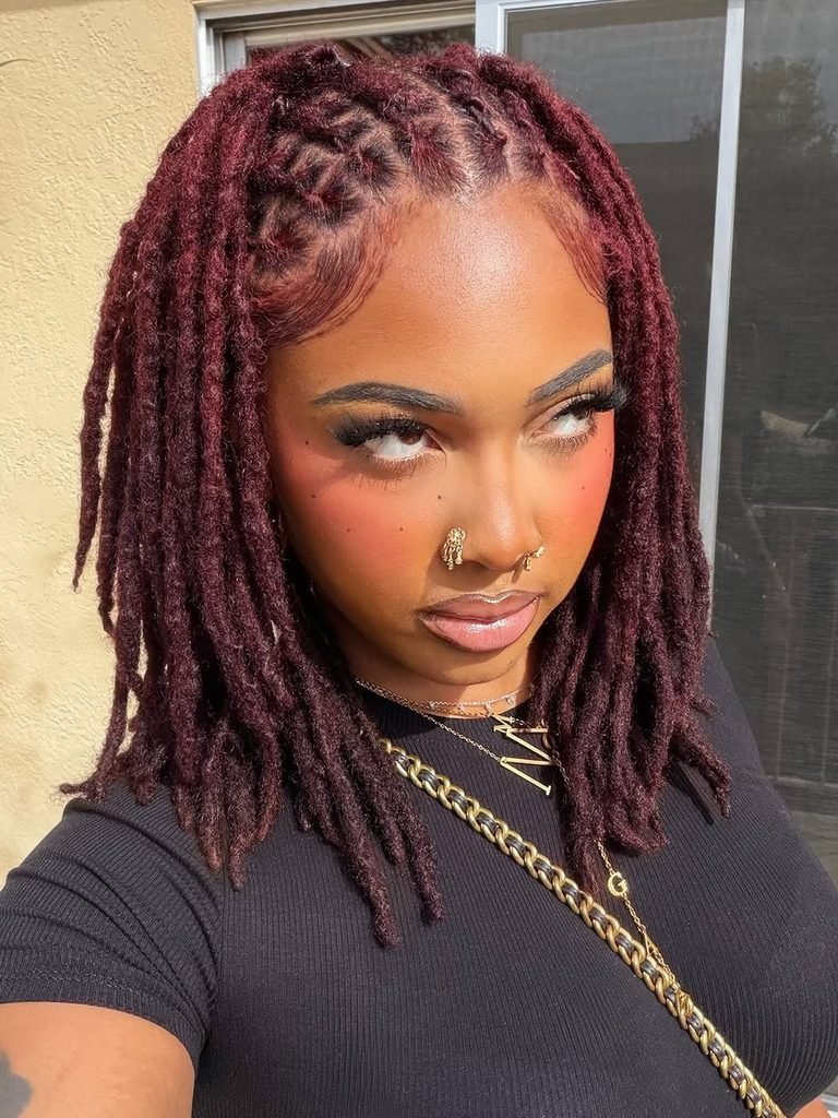 woman with shoulder-length burgundy locs featuring a braided half-up style