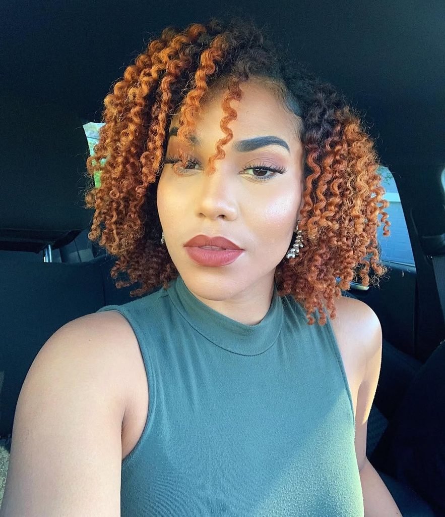 woman in a car showing a shoulder-length curly bob with caramel highlights