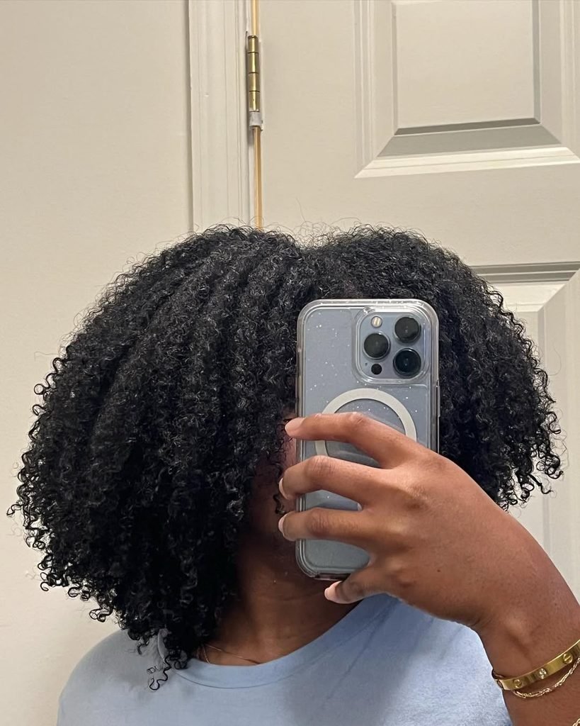 woman holding a smartphone covering her face showing voluminous kinky curly hair