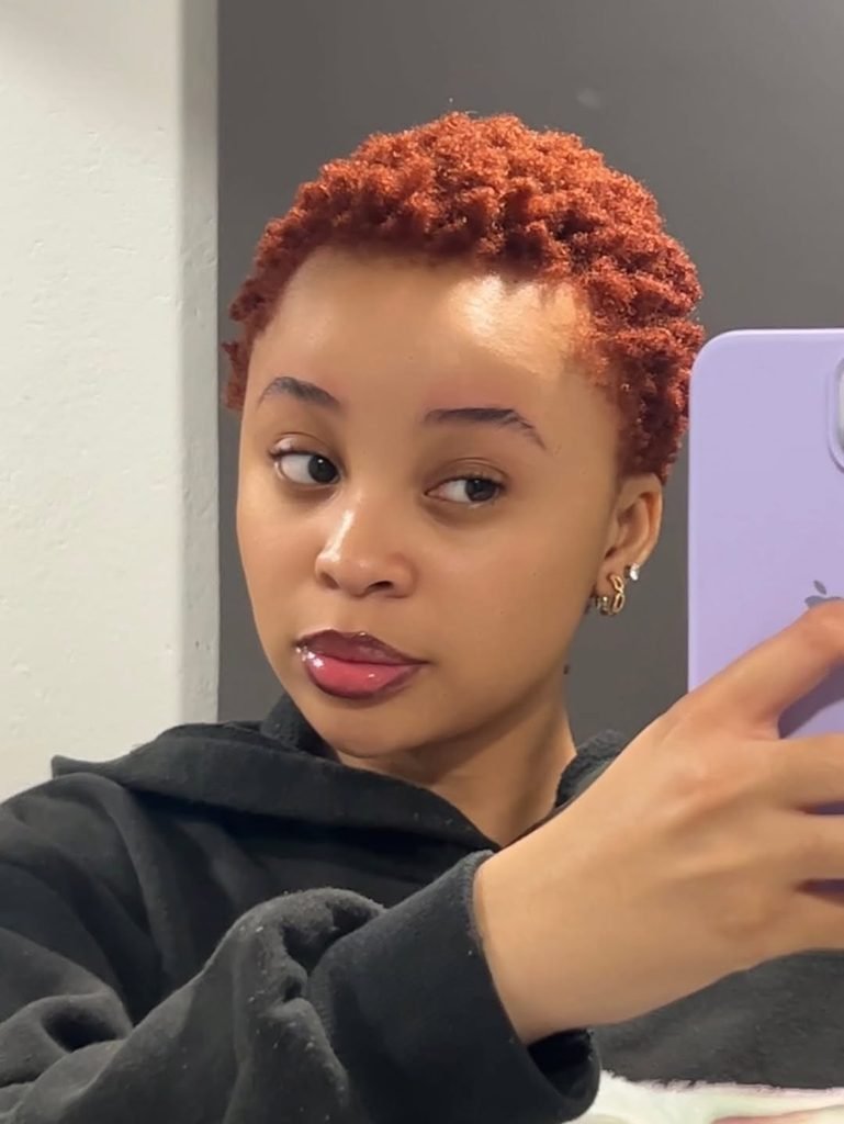 woman with a short, bright copper-colored tapered afro haircut taking a mirror selfie