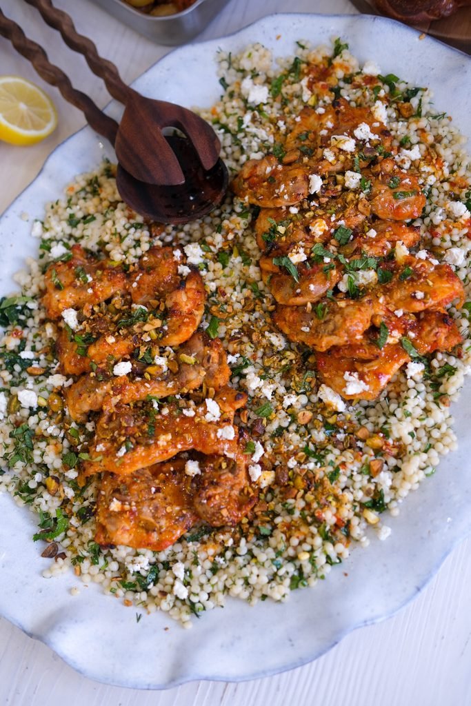 harissa roasted chicken legs served over a large platter of couscous with herbs