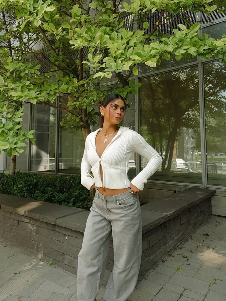 woman wearing a white hooded zip-up sweater and grey wide-leg jeans outdoors
