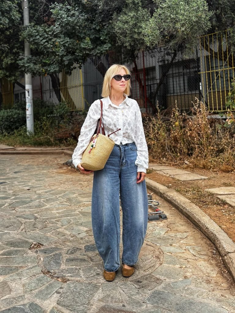 woman wearing a white textured shirt, baggy blue jeans, and carrying a straw bag