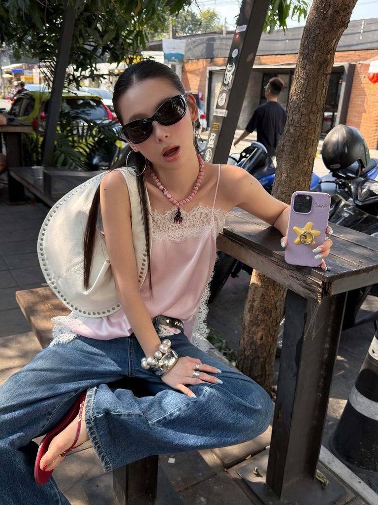 woman wearing a pink satin camisole and wide-leg blue jeans sitting outdoors at a table
