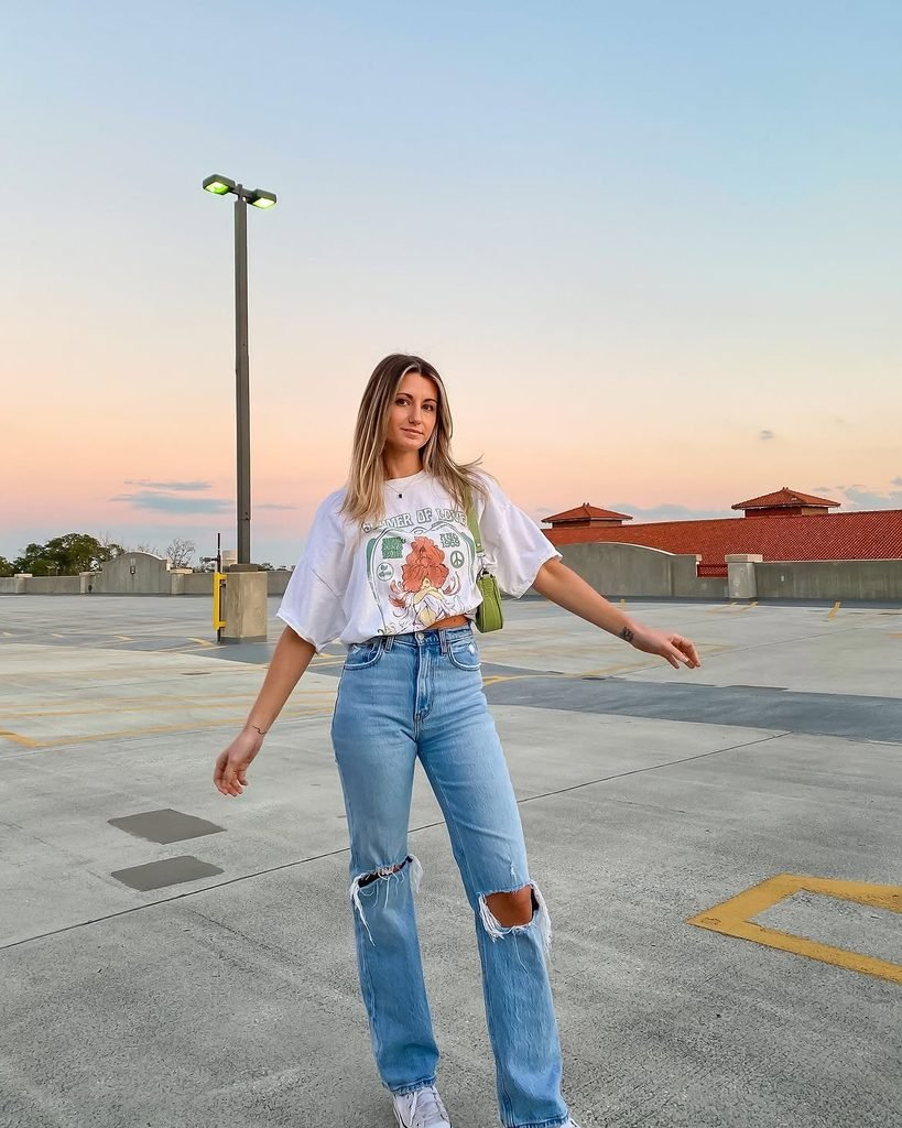 woman wearing a white graphic t-shirt and ripped light wash jeans on a rooftop