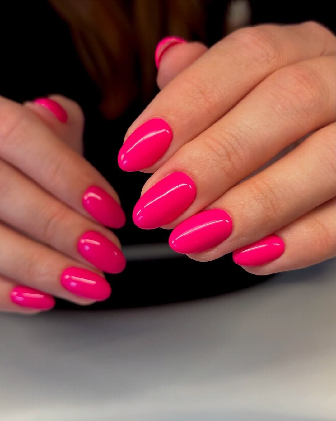 two hands displaying a solid bright fuchsia pink summer manicure on short oval nails
